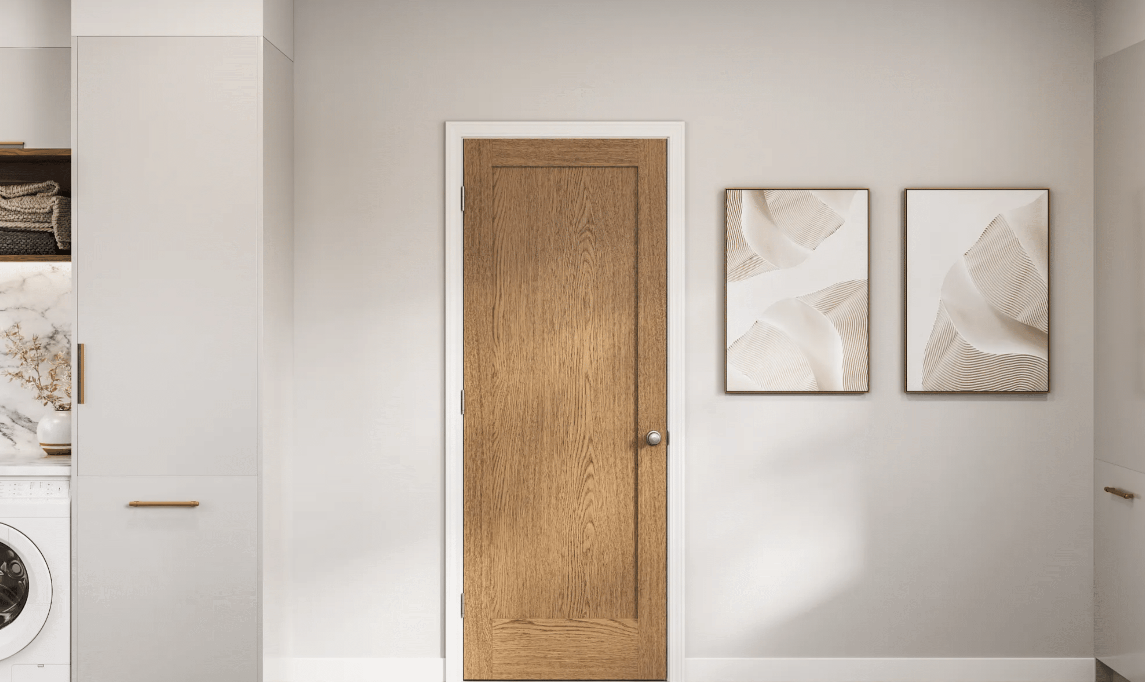 A wooden door with a silver knob is centered on a light gray wall. To the right, two framed abstract art pieces hang side by side. To the left, part of a laundry area with a washing machine and shelves is visible.