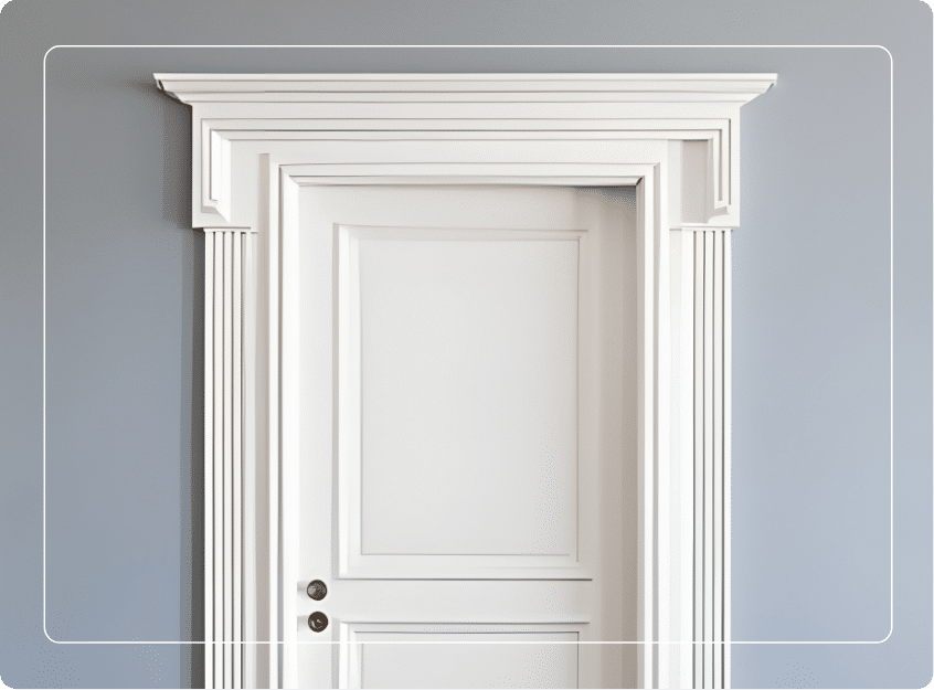 A white door with a decorative, classic-style frame and molding stands against a light gray wall. There are two brass door knobs, and the image has rounded white lines framing its edges.